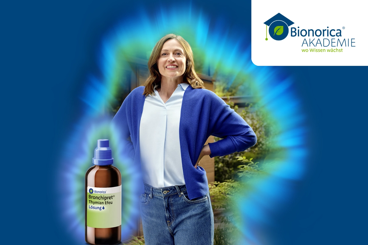 Frau steht lächelnd mit Händen in die Hüfte gestützt, eine Flasch Bronchipret daneben, dahinter ein strahlender Glow-Effekt