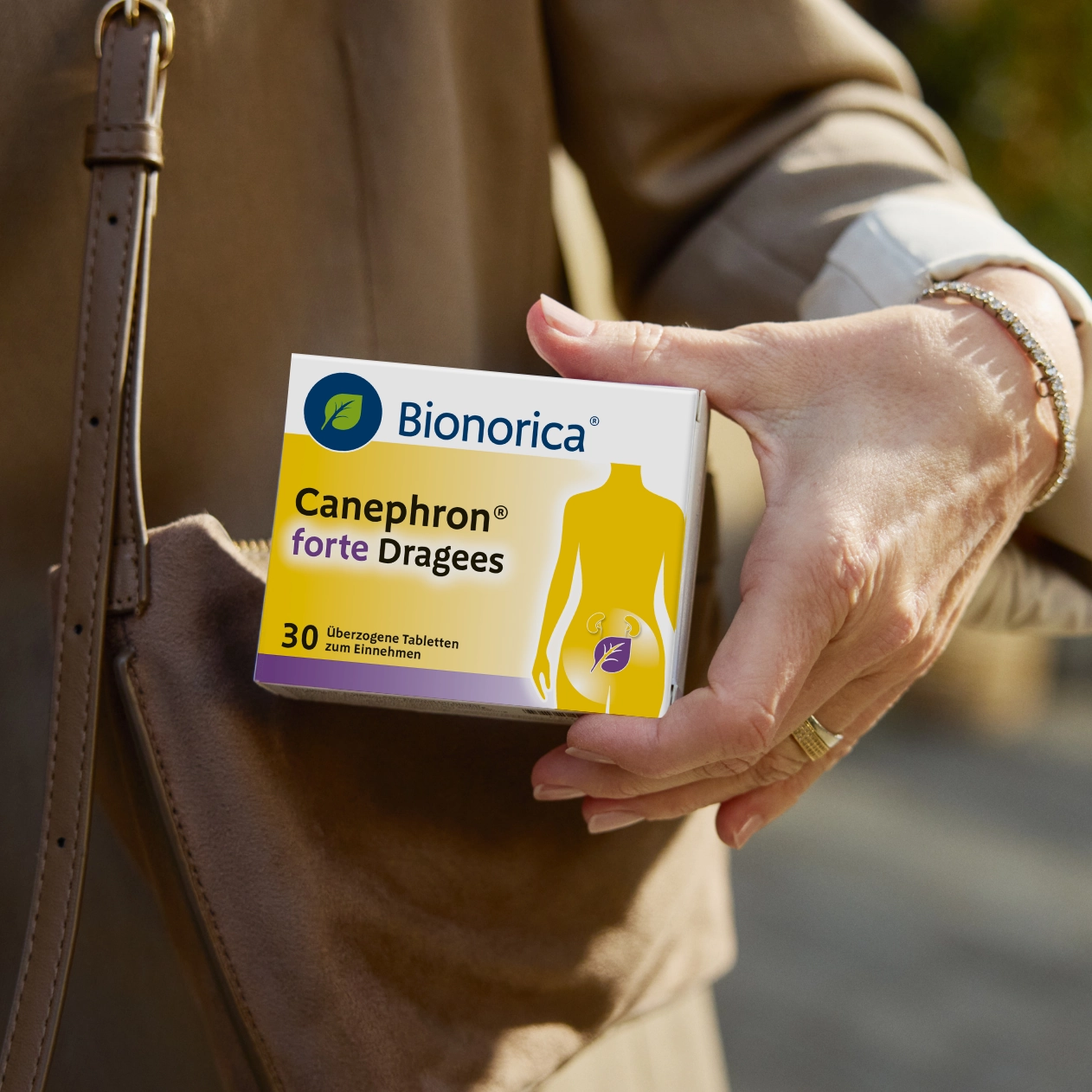 Hand hält Canephron vor einer Tasche