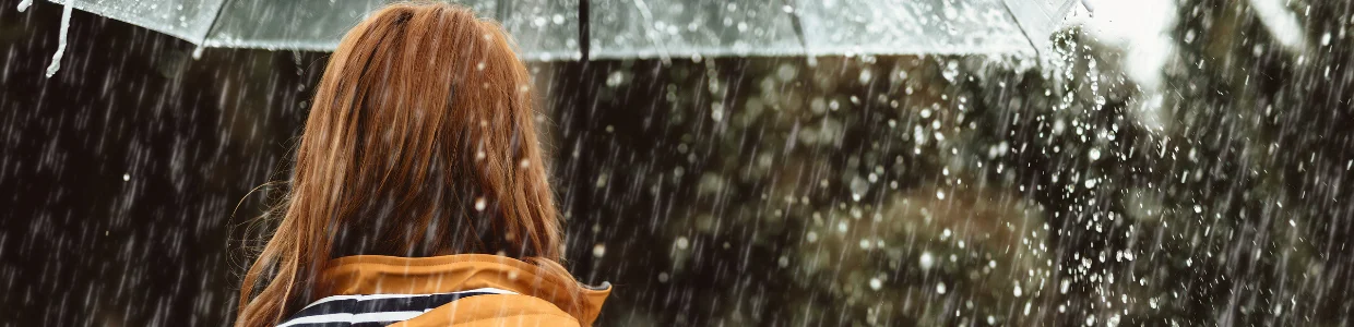 Frau geht mit Regenschirm im Regen spazieren - Symbolbild für Unterleibsschmerzen ohne Periode