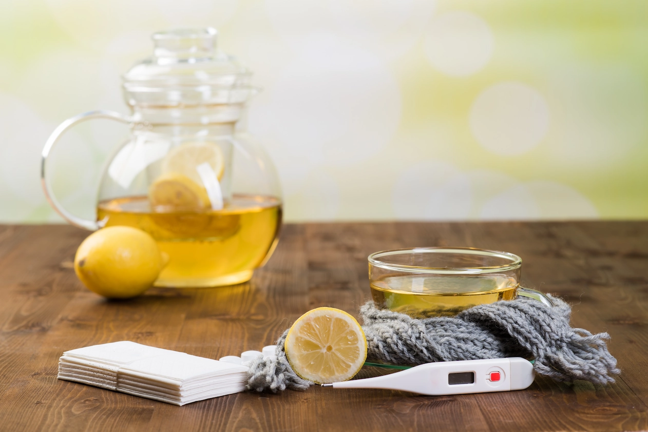 Tee, Zitrone, Taschentücher und  Thermometer auf einem Tisch