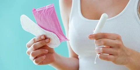 Frau hält Binde und Tampon vor türkisfarbenem Hintergrund – Symbolbild für starke Regelblutung bzw. starke Periode