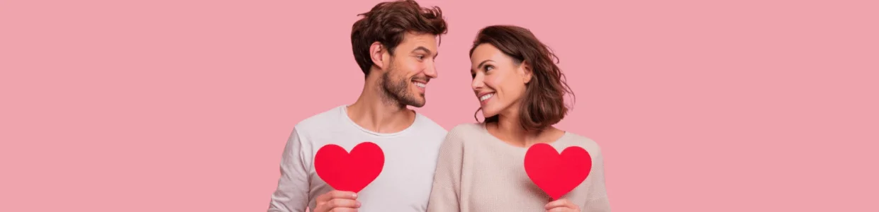 Zwei Personen mit roten Papierherzen vor rosa Hintergrund – Symbolbild für hormonfreie Verhütung.