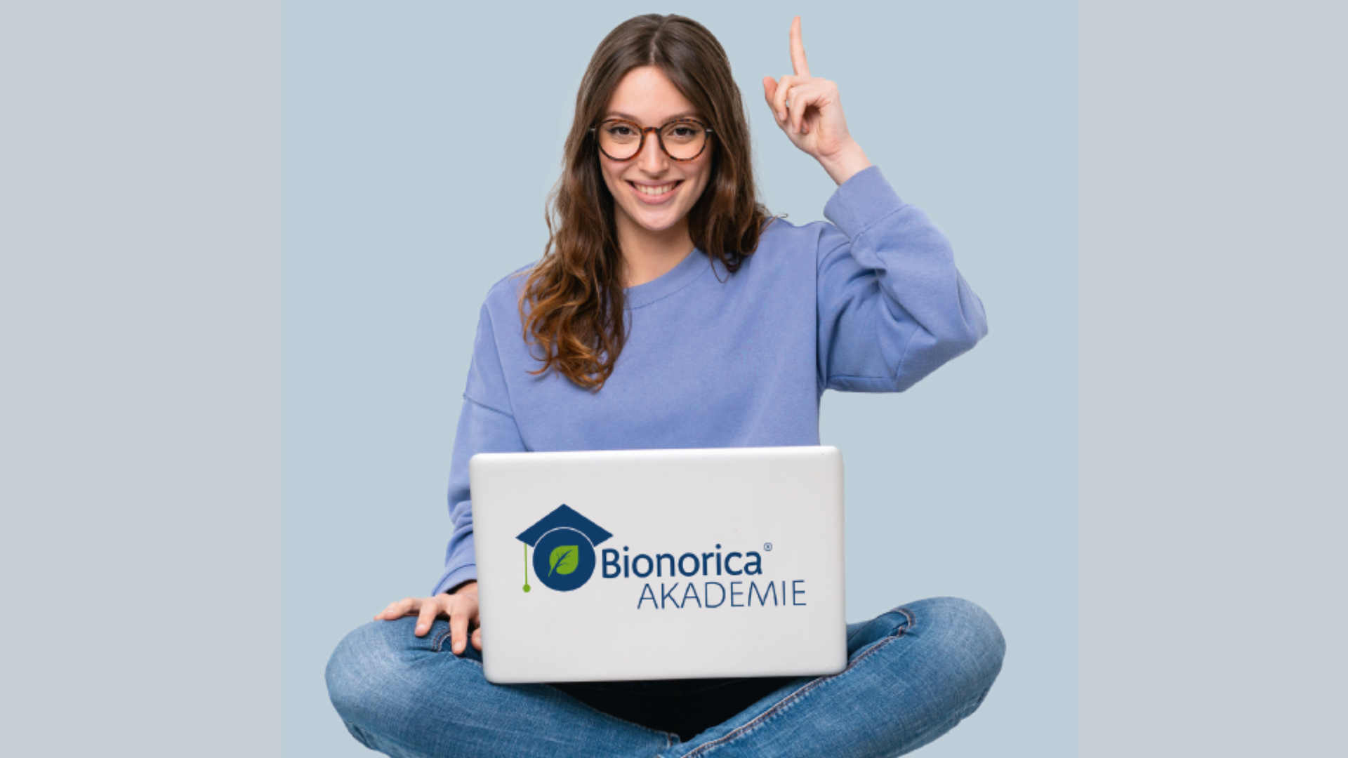 Darstellung einer Frau am Laptop, sie lächelt und zeigt mit dem linken Finger in die Luft.