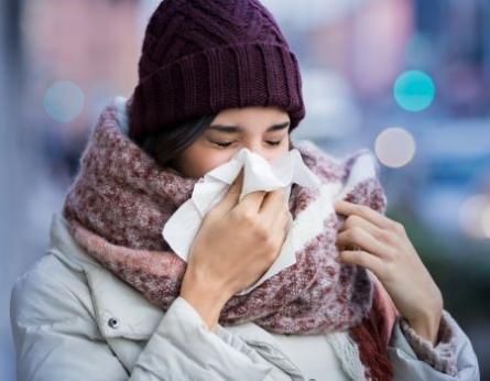 Frau mit Schnupfen putzt sich die Nase in winterlicher Straßen-Atmosphäre